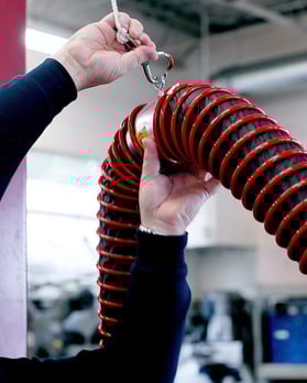 Overhead vehicle exhaust removal system in auto repair shop capturing tailpipe emissions at the source.