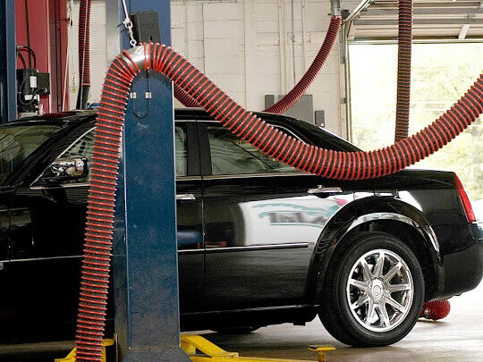 A passenger vehicle in a bay shown behind an overhead exhaust removal system.