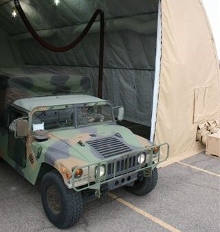A military humvee in the entrance of a repair tent with an overhead exhaust removal system shown in the background.