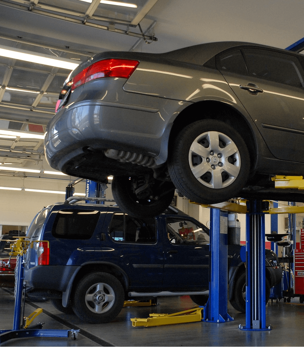 An SUV and a passenger vehicle on a lifted platform shown in an auto repair and maintenance shop.